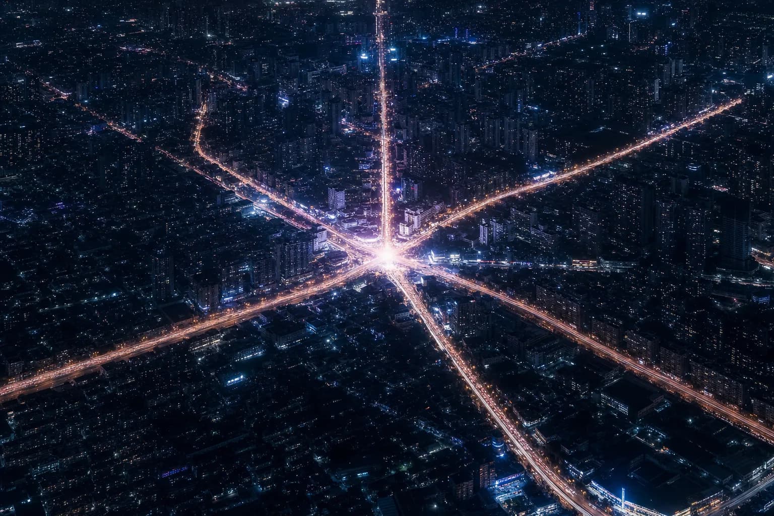 Aerial night view of a city where streets glow like a network of light trails converging on one node